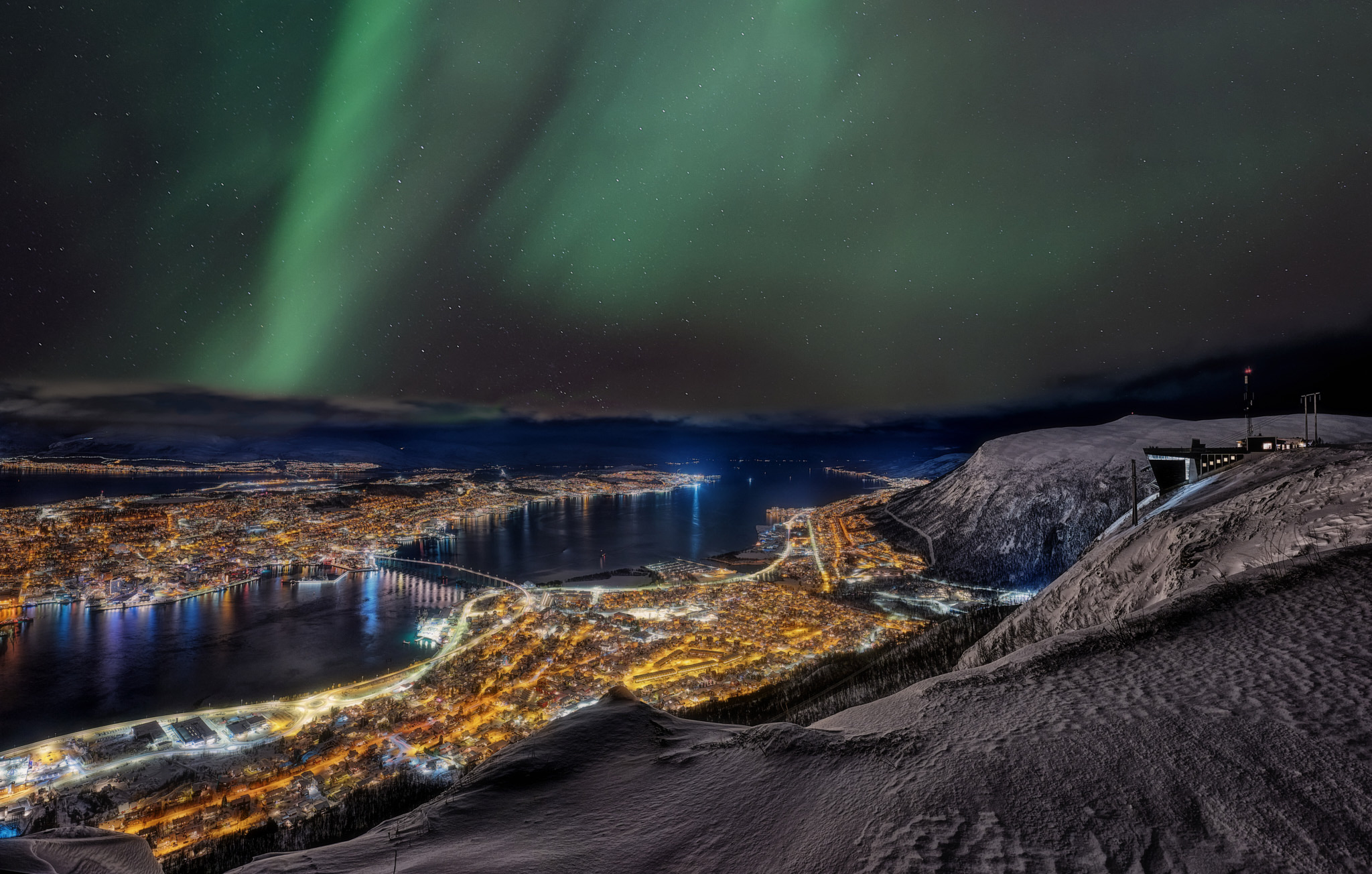 Nordlichter über Tromsø mit Blick auf die beleuchtete Stadt und den Fjord